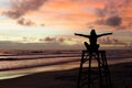 A silhouette woman sitting on a lifeguard tower with open arms enjoying the sunrise on a beach and the sun`s rays painting the sky Royalty Free Stock Photo