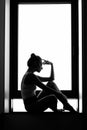 Silhouette of a woman sitting thinking on a window sill. Black and white photography. loneliness Royalty Free Stock Photo