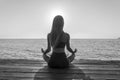 Silhouette of woman sitting at yoga pose on the tropical beach during sunset. Girl practicing yoga near sea water. Black and white Royalty Free Stock Photo