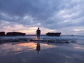 Silhouette of a woman standing alone from behind on rocky beach at sunset with dramatic clouds over the sea. Royalty Free Stock Photo