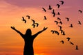 Silhouette woman standing raised up hands during flock of lesser whistling duck flying on sunset