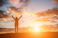 Silhouette woman at sunset standing elated with arms raised up a