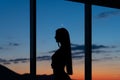 Silhouette Of Woman In Sunshine At Window With View On Sunset In Mountains