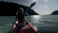 Silhouette of woman tourist raising hands while sailing in canoe along sea bay water to distant hilly island backside Royalty Free Stock Photo