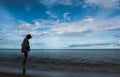 Silhouette woman walking on seabeach in evening with beautiful blue sky over sea water, look lonely and quiet.