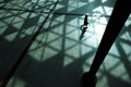 Silhouette of a woman walking in shadows cast by sunlight coming through a moder glass roof. Top view background