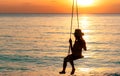 Silhouette woman wear bikini and straw hat swing the swings at the beach on summer vacation at sunset. Enjoying and relaxing girl Royalty Free Stock Photo