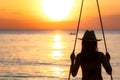 Silhouette woman wear bikini and straw hat swing the swings at the beach on summer vacation at sunset. Enjoying and relaxing girl Royalty Free Stock Photo