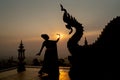 Silhouette of woman wear Thai traditional dress and stand with Thai dance in front of naga sculpture in temple with sunrise in Royalty Free Stock Photo