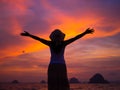 Silhouette of woman wearing hat with open arms under the sunrise near the sea