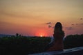 Silhouette of a women in dress sitting on stone on top of hill. She views red sun circle falling down Royalty Free Stock Photo