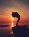 Silhouette yoga girl by the beach at sunrise doing standing pose Royalty Free Stock Photo