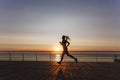 Silhouette of a young beautiful athletic girl with long blond hair in headphones, who listens to music and runs at dawn over the s