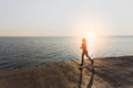 Silhouette of a young beautiful athletic girl with long blond hair in headphones, who listens to music and runs at dawn over the s