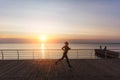 Silhouette of a young beautiful athletic girl with long blond hair in headphones, who listens to music and runs at dawn over the s