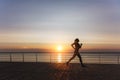 Silhouette of a young beautiful athletic girl with long blond hair in headphones, who listens to music and runs at dawn over the s