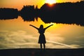 Silhouette of a young beautiful girl with hands up against the background of the sunset in the reflection of the pond Royalty Free Stock Photo