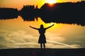 Silhouette of a young beautiful girl with hands up against the background of the sunset in the reflection of the pond Royalty Free Stock Photo