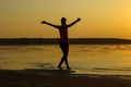 Silhouette of a young beautiful girl with hands up against the background of the sunset in the reflection of the sea coast Royalty Free Stock Photo