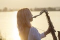 Silhouette of a young beautiful girl playing the saxophone at sunrise by the river, woman on the nature at sunrise giving a