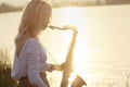 Silhouette of a young beautiful girl playing the saxophone at sunrise by the river, woman on the nature at sunrise giving a