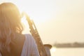 Silhouette of a young beautiful girl playing the saxophone at sunrise by the river, woman on the nature at sunrise giving a