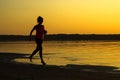 Silhouette of a young beautiful girl is running along the seashore on the orange sunset background Royalty Free Stock Photo