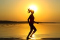 Silhouette of a young beautiful girl is running along the seashore on the orange sunset background Royalty Free Stock Photo