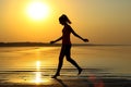 Silhouette of a young beautiful girl walking along the seashore during orange sunset Royalty Free Stock Photo