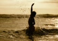 Silhouette of young boy playing crazy happy and free at the beach splashing with water playing with sea waves jumping and having