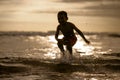 Silhouette of young boy playing crazy happy and free at the beach splashing with water playing with sea waves jumping and having