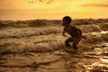 Silhouette of young boy playing crazy happy and free at the beach splashing with water playing with sea waves jumping and having