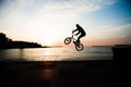 Silhouette of young caucasian biker jumping on sea coast in city on sunset sky background Royalty Free Stock Photo