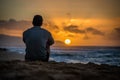 Silhouette of young caucasian male sitting on Sunset Beach looking out at sunset over the ocean