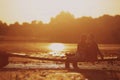 Silhouette of young couple in love are sitting and hugging on the wooden bridge outdoors near the lake at sunset on summer. Royalty Free Stock Photo