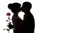 Silhouette of a young couple in love on white isolated background, man kissing woman and holding rose flower, concept love Royalty Free Stock Photo