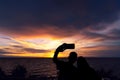 A silhouette of a young couple taking a picture with the sunset at Noen Nang Phaya viewpoint in Chanthaburi, Thailand