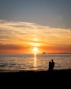 The silhouette of a young couple walking along the Lomma beach while the sun sets behind the nuclear power plant BarsebÃÂ¤ck Royalty Free Stock Photo