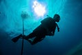 Silhouette of young diver against Sun light at the sea surface and hanging down steel anchor chain. Air bubbles from breathing.