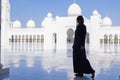 Silhouette of young elegant girl - traveler in traditional muslim dress and hijab standing on backdrop of Grand White Mosque