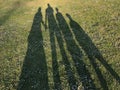 Silhouette of a young family on green grass in the park casted by a long shadow. Concept of happiness and celebrating family live Royalty Free Stock Photo