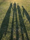 Silhouette of a young family on green grass in the park casted by a long shadow. Concept of happiness and celebrating family live Royalty Free Stock Photo