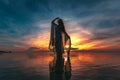 Silhouette of young fashionable woman standing in water on the beach at sunset Royalty Free Stock Photo