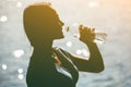 Silhouette of a young female athlete in tracksuit drinking water from a bottle on the beach in summer, during morning exercises. Royalty Free Stock Photo