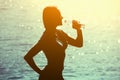 Silhouette of a young female athlete in tracksuit drinking water from a bottle on the beach in summer, Royalty Free Stock Photo