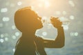 Silhouette of a young female athlete in tracksuit drinking water from a bottle on the beach in summer during morning exercises. Royalty Free Stock Photo