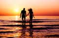 Silhouette of young fitness couple walking inside the water at sunrise - Multi race people having fun on vacation - Romantic and Royalty Free Stock Photo