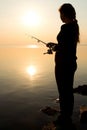 Silhouette of a young girl fishing at sunset near the sea Royalty Free Stock Photo