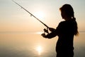 Silhouette of a young girl fishing at sunset near the sea Royalty Free Stock Photo