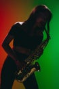 Silhouette of young girl with saxophone posing isolated on green-red background.
